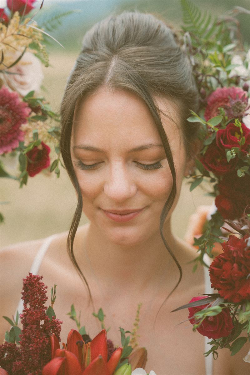 Bride's face framed by an arch of burgundy and blush blooms, her eyes lowered in a quiet smile